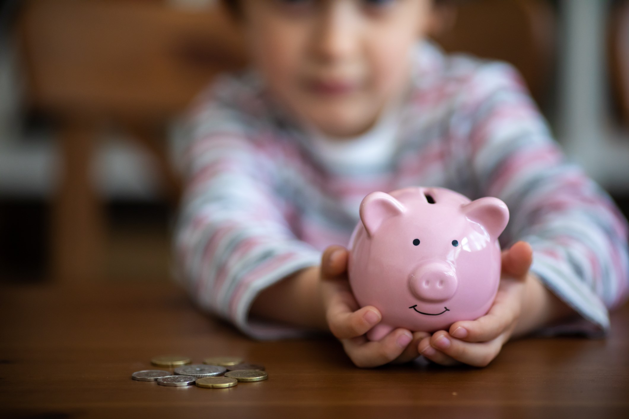 Child holding a piggy bank, coins on a table
