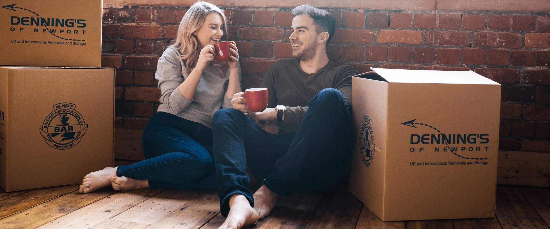 Couple sitting on wooden floor, drinking coffee, moving boxes