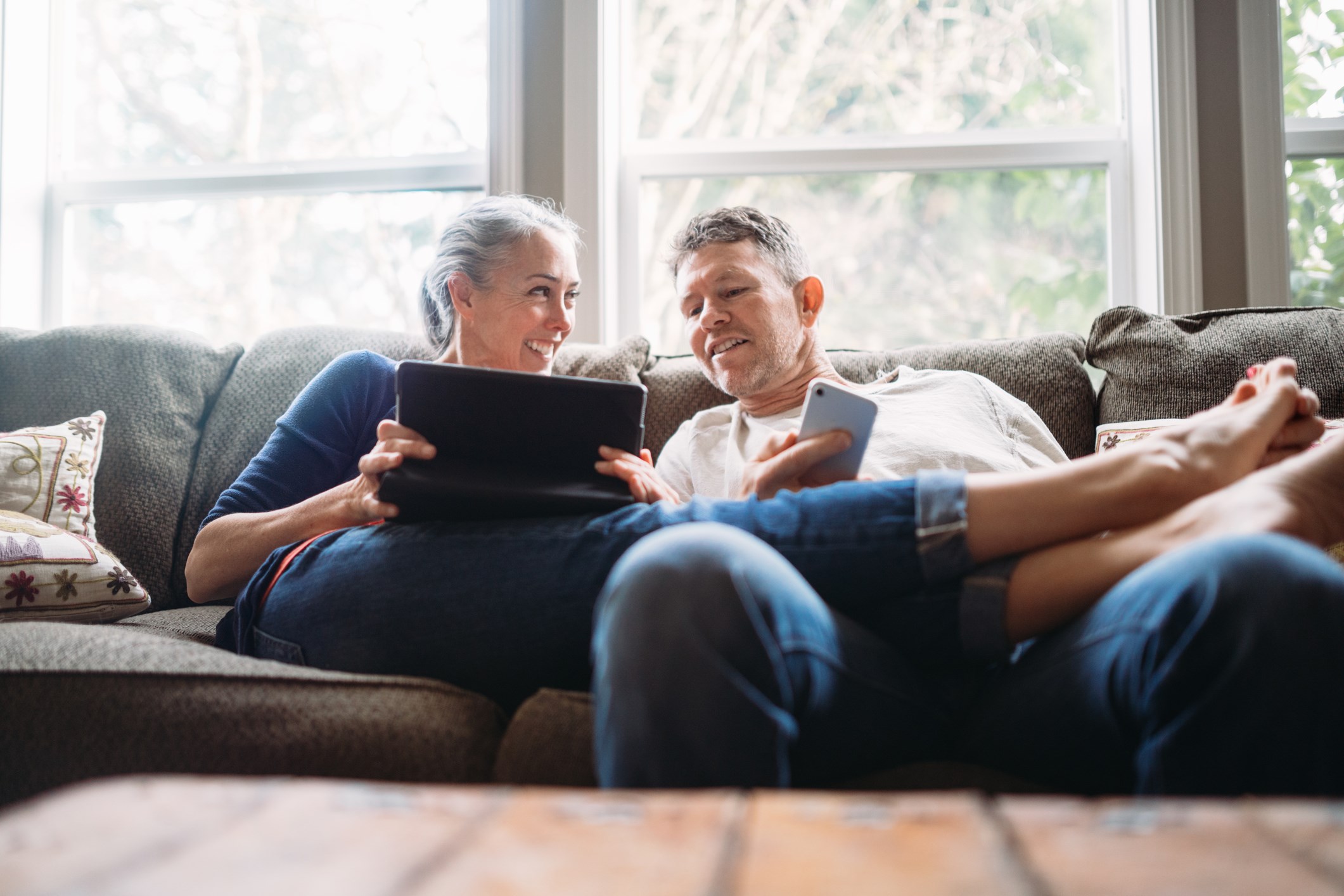Couple on sofa, looking at tablet and mobile phone